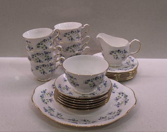 May include: A vintage tea set featuring white porcelain cups, saucers, and a creamer, adorned with delicate blue floral patterns and gold trim. The set includes teacups, saucers, and a serving platter, perfect for a tea party.