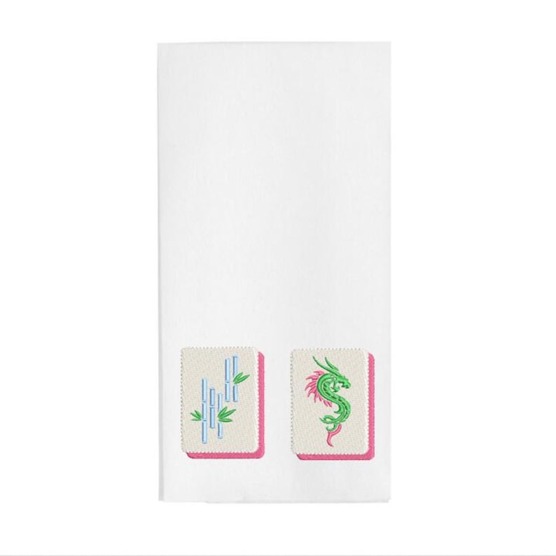 May include: White rectangular towel featuring embroidered Mahjong tiles. One tile shows bamboo stalks in blue and green, the other a green dragon with pink accents. Both tiles have a pink border.
