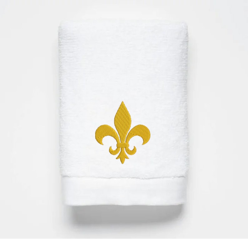 May include: White bath towel with a gold embroidered fleur-de-lis design.