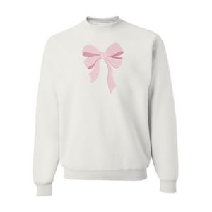 Peut inclure: Un sweat-shirt blanc &agrave; manches longues et col rond, orn&eacute; d'un n&oelig;ud rose clair brod&eacute; au centre. Le v&ecirc;tement pr&eacute;sente un col, des poignets et un ourlet c&ocirc;tel&eacute;s, offrant une apparence nette et structur&eacute;e avec un &eacute;l&eacute;ment d&eacute;coratif central.