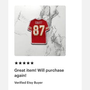 May include: A red and gold patch in the shape of a football jersey. The jersey patch has the name "SWIFT" above the number "87". The patch is on a white and gray marble-like background. The text "Great item! Will purchase again!" is below the patch.