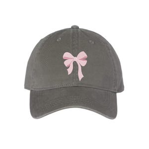 Peut inclure: Une casquette de baseball gris anthracite orn&eacute;e d'un n&oelig;ud rose clair brod&eacute; au centre du panneau avant. La casquette pr&eacute;sente une calotte structur&eacute;e, une visi&egrave;re incurv&eacute;e et des &oelig;illets cousus pour la ventilation, offrant un design &eacute;pur&eacute;.