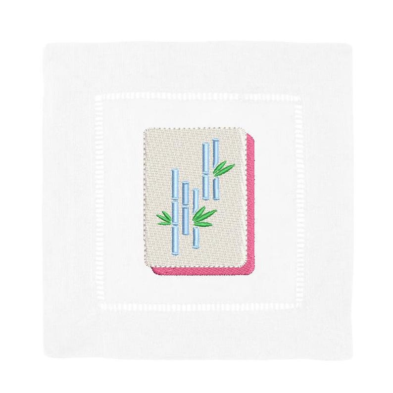 May include: White square linen cocktail napkin with a stitched border. The napkin features an embroidered design of bamboo stalks in blue and green, set against a beige background with a pink border.