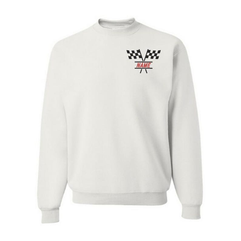 May include: A white crewneck sweatshirt featuring a racing theme. The design includes two black and white checkered flags above the word "NAME" in red, with a red line underneath. The sweatshirt has long sleeves and a ribbed hem.