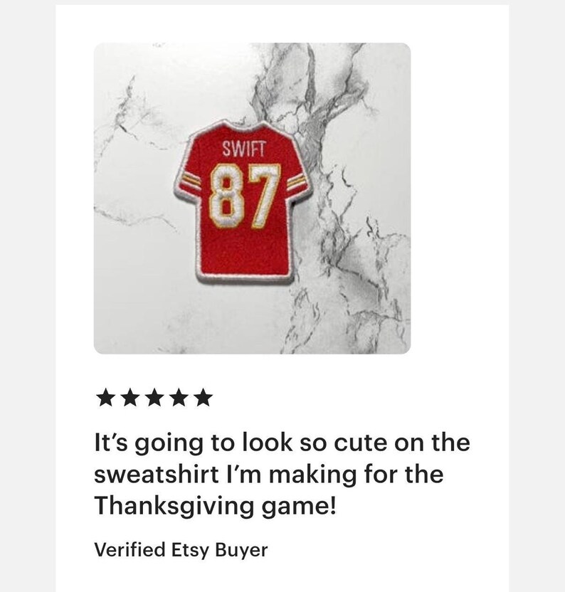 May include: Red and gold jersey patch with the name "SWIFT" and the number "87". The patch is designed to resemble a football jersey. The background is a white and gray marble pattern.