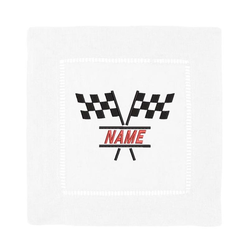 May include: White square linen cocktail napkin with embroidered racing flags and the word "NAME" in red. The flags are black and white checkered. The napkin has a stitched border.