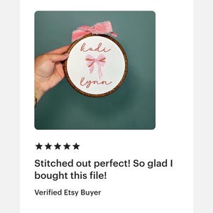 Peut inclure: Un tambour &agrave; broder circulaire en bois contenant un tissu blanc avec le texte brod&eacute; 'kodi lynn' en police cursive et un motif de n&oelig;ud rose central. Un ruban rose effiloch&eacute; est attach&eacute; au sommet du tambour pour le suspendre.