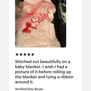 Peut inclure: Une couverture pour b&eacute;b&eacute; en fausse fourrure rose p&acirc;le, enroul&eacute;e et nou&eacute;e avec un ruban en organza rose translucide. Le pr&eacute;nom Salem est brod&eacute; en lettres cursives rouges sur le tissu, accompagn&eacute; d'un petit n&oelig;ud rouge pr&egrave;s de l'inscription.