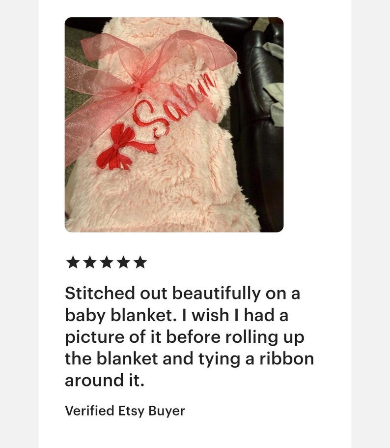 Peut inclure: Une couverture pour b&eacute;b&eacute; en fausse fourrure rose p&acirc;le, enroul&eacute;e et nou&eacute;e avec un ruban en organza rose translucide. Le pr&eacute;nom Salem est brod&eacute; en lettres cursives rouges sur le tissu, accompagn&eacute; d'un petit n&oelig;ud rouge pr&egrave;s de l'inscription.