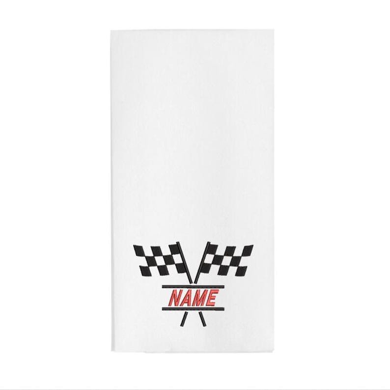 May include: White rectangular towel with a black and white checkered flag design and the word "NAME" in red. The towel has a racing theme.