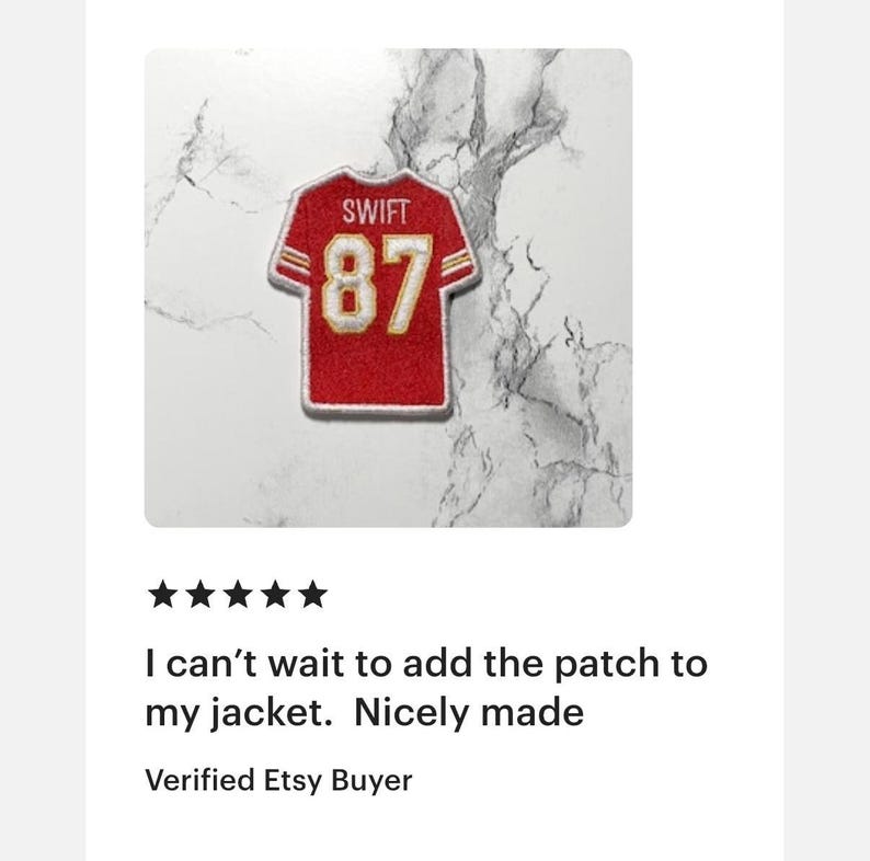 May include: Red and gold embroidered patch in the shape of a football jersey. The patch features the name "SWIFT" above the number "87". The patch is on a white background with a marble pattern. The text "I can't wait to add the patch to my jacket. Nicely made" is below the patch.