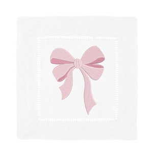 Peut inclure: Une serviette carr&eacute;e en lin blanc avec un n&oelig;ud rose clair brod&eacute; au centre. La serviette pr&eacute;sente une bordure d&eacute;corative &agrave; jour qui encadre la zone centrale o&ugrave; le n&oelig;ud est positionn&eacute;. Le tissu a un aspect propre et net.