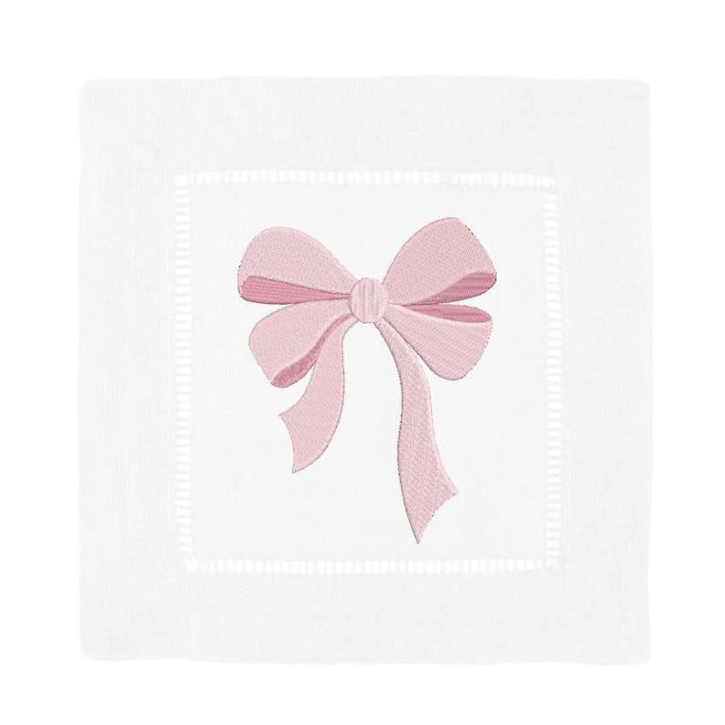 Peut inclure: Une serviette carr&eacute;e en lin blanc avec un n&oelig;ud rose clair brod&eacute; au centre. La serviette pr&eacute;sente une bordure d&eacute;corative &agrave; jour qui encadre la zone centrale o&ugrave; le n&oelig;ud est positionn&eacute;. Le tissu a un aspect propre et net.