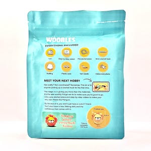 May include: A teal package labeled "WOOBLES" contains a crochet kit. The package lists included items: yarn, step-by-step videos, a pre-started piece, a 4mm crochet hook, stuffing, plastic eyes, a yarn needle, and online instructions. The finished size is 4.5 inches.