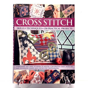 May include: A hardcover book titled "CROSS STITCH" with the subtitle "SKILLS • TECHNIQUES • 150 PRACTICAL PROJECTS." The cover features a colorful cross-stitched pillow and other cross-stitch examples. The book is on a white background.