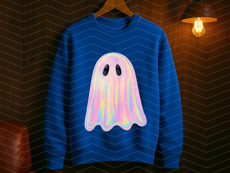 Puede incluir: Una sudadera azul con un dise&ntilde;o de fantasma hologr&aacute;fico. El fantasma tiene un acabado nacarado e iridiscente con ojos ovalados negros. La sudadera est&aacute; colgada de una percha de madera contra una pared de paneles de madera oscura.