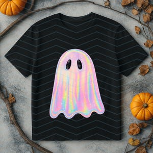 Puede incluir: Camiseta negra con un dise&ntilde;o de fantasma hologr&aacute;fico. El fantasma tiene un acabado nacarado e iridiscente con ojos ovalados negros. La camiseta est&aacute; decorada con un patr&oacute;n de chevr&oacute;n. Dos peque&ntilde;as calabazas y ramas con hojas est&aacute;n en el fondo.
