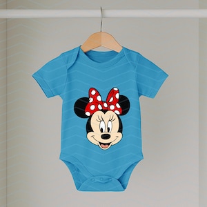 May include: A light blue baby onesie featuring a Minnie Mouse graphic. The onesie has short sleeves and a round neckline. The Minnie Mouse graphic includes a red bow with white polka dots. The onesie is hanging on a wooden hanger.