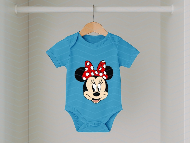 May include: A light blue baby onesie featuring a Minnie Mouse graphic. The onesie has short sleeves and a round neckline. The Minnie Mouse graphic includes a red bow with white polka dots. The onesie is hanging on a wooden hanger.