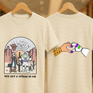 Pu&ograve; includere: T-shirt beige con un'illustrazione a cartoni animati di due personaggi, un cowboy e un ranger spaziale. La parte anteriore della maglietta ha la scritta "YOU GOT A FRIEND IN ME". Il retro della maglietta mostra mani che formano un cuore.