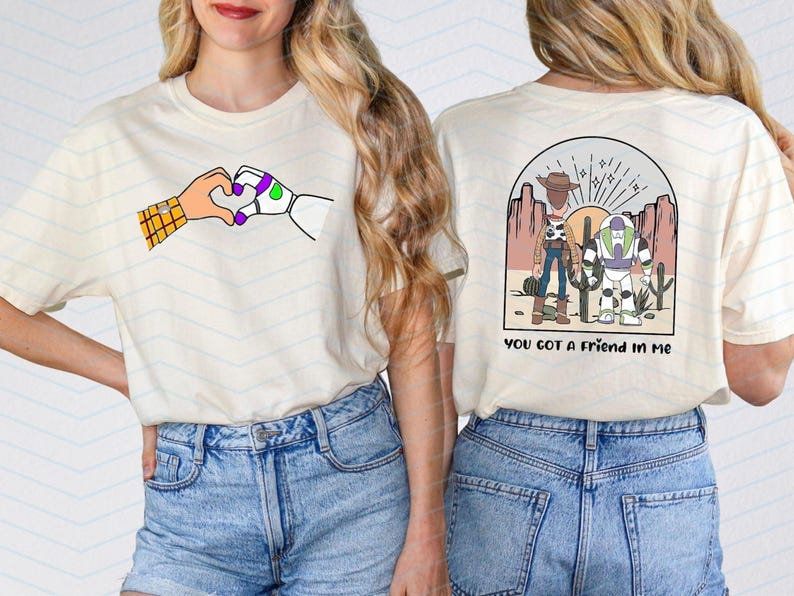 Pu&ograve; includere: T-shirt color crema con un'illustrazione a cartoni animati di due mani che formano un cuore. Una mano &egrave; un robot, l'altra un cowboy. Il retro della maglietta presenta una scena del deserto con personaggi dei cartoni animati e la scritta "YOU GOT A FRIEND IN ME."