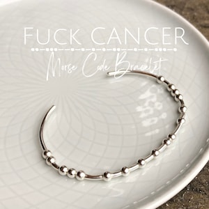 May include: Silver bracelet with a message in Morse code. The bracelet reads "FUCK CANCER" in Morse code.
