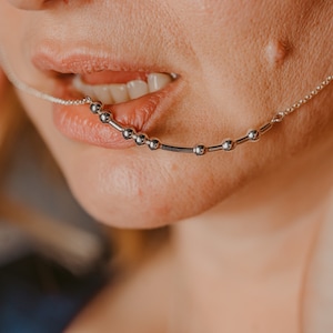 May include: A close-up of a person's mouth with a silver chain with small round beads going through their lip.