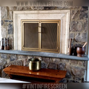 May include: A gold metal fireplace screen with a mesh design and two doors. The screen is installed in a stone fireplace with a wooden mantle. The text "#VINTINFIRESCREEN" is visible at the bottom of the image.