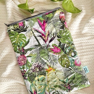 May include: A rectangular, quilted pouch with a tropical floral pattern. The design features large green leaves, pink and purple flowers, and a white background. A small, light blue tag is visible on the lower right corner. The pouch has a gray zipper.
