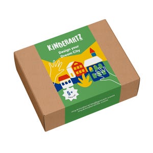 Może przedstawiać: Brązowe kartonowe pudełko z zieloną etykietą z napisem "KINDERARTZ Design your Dream City". Etykieta zawiera kolorowe ilustracje domów i rąk. Pudełko jest dla dzieci w wieku 5+ lat.