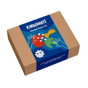 May include: A rectangular cardboard box with a blue label featuring the text "KINDERARTZ Marble Paper 2.0". The label includes colorful abstract shapes, hand illustrations, and the age range "9-12 years old". The box is designed for children's art projects.