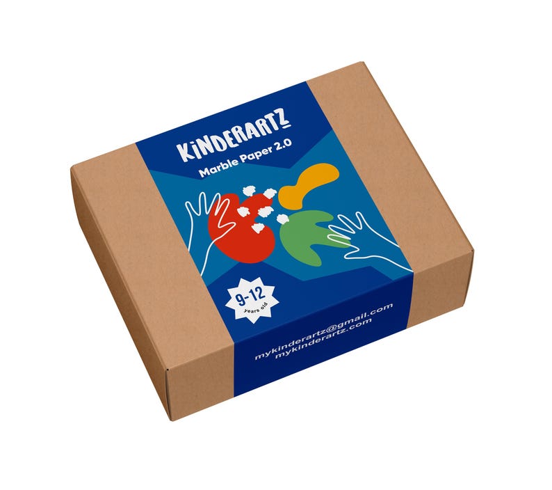 May include: A rectangular cardboard box with a blue label featuring the text "KINDERARTZ Marble Paper 2.0". The label includes colorful abstract shapes, hand illustrations, and the age range "9-12 years old". The box is designed for children's art projects.