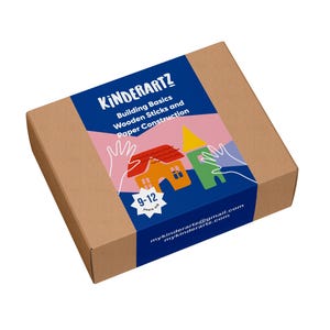May include: A brown cardboard box with a blue label. The label reads "KINDERARTZ" and "Building Basics Wooden Sticks and Paper Construction." There are illustrations of houses and hands. The box is designed for children aged 9-12 years.