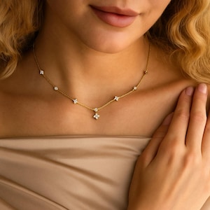 May include: A gold necklace with small, sparkling gemstones and a floral pendant. The necklace is worn on a person's neck. The gemstones are round and clear, adding a touch of elegance. The chain is visible against the skin.