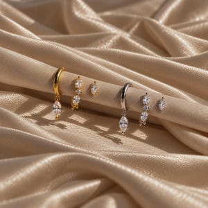 May include: A set of six earrings featuring two gold-tone hoop earrings with marquise-cut clear stones, two gold-tone huggie earrings with three marquise-cut stones, two silver-tone hoop earrings with marquise-cut stones, and two silver-tone studs.