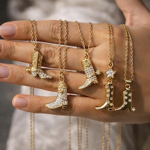Puede incluir: Una colección de collares dorados, cada uno con un colgante con forma de bota de vaquero. Algunas botas están adornadas con cristales transparentes, mientras que otras tienen un acabado dorado liso. Los colgantes cuelgan de delicadas cadenas doradas.