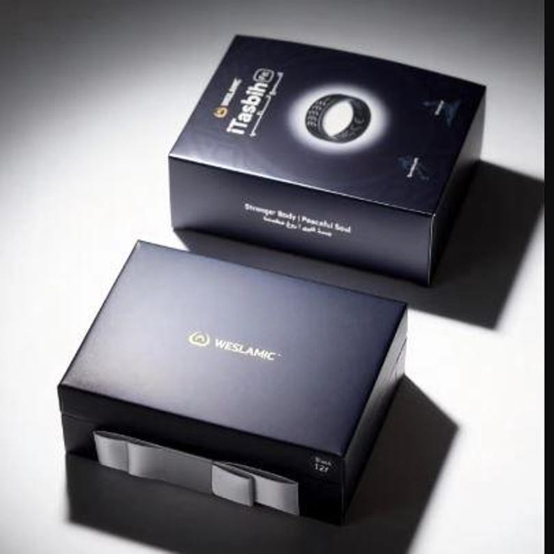 May include: Two dark blue rectangular product boxes. The top box features the text iTasbih, an image of a black ring, and the phrase Stronger Body | Peaceful Soul. The bottom box displays the WESLAMIC logo and a grey ribbon pull tab on the front.