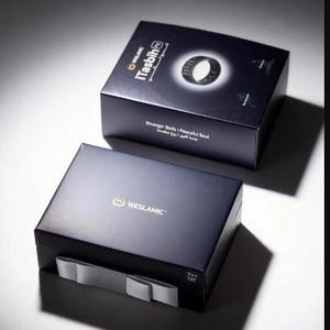 May include: Two dark blue rectangular product boxes. The top box features the text iTasbih, an image of a black ring, and the phrase Stronger Body | Peaceful Soul. The bottom box displays the WESLAMIC logo and a grey ribbon pull tab on the front.