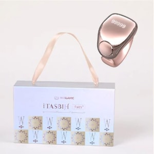Può includere: Un contatore digitale color oro rosa con il numero 99999, accanto a una scatola bianca con un manico a nastro. La scatola presenta la scritta "iTASBIH Faith" e un motivo a stelle ripetute.