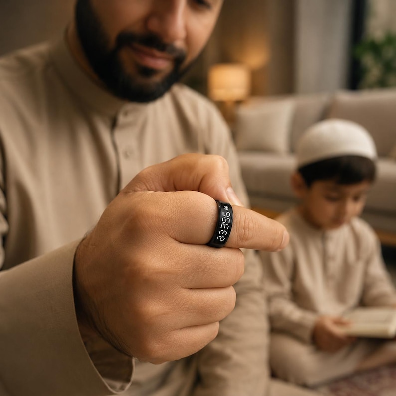 May include: A black digital ring featuring a small screen displaying the white numerical text 23:35. The band has a smooth, matte finish and is worn on a finger. The device is a wearable electronic accessory designed to show the current time clearly.