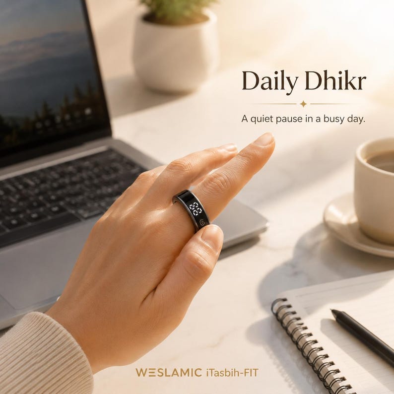 May include: A black digital smart ring with a small screen displaying numbers, worn on a finger. The text Daily Dhikr, A quiet pause in a busy day, and WESLAMIC iTasbih-FIT are visible in the image, alongside a laptop, a cup, and a notebook.