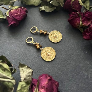 May include: Gold hoop earrings with a round, ornate pendant and brown beads hanging from the bottom.