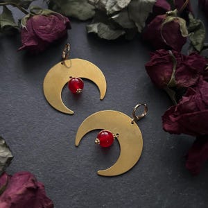 May include: A pair of gold crescent moon earrings with red gemstone accents.