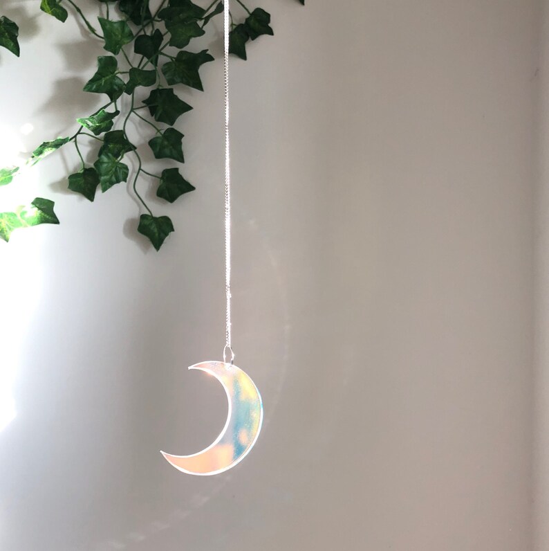 May include: A silver chain hangs from the ceiling with a iridescent crescent moon shaped ornament at the end.
