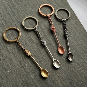 May include: Four decorative spoon keyrings in gold, silver, and copper tones. Each spoon features a crown design and is attached to a keyring. The spoons vary in colour and chain style, offering a unique accessory.