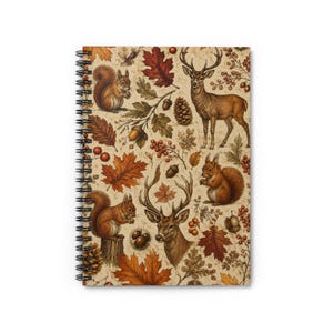 Pode incluir: Um caderno de espiral com um padrão repetitivo de esquilos castanhos, veados, pinhas, bolotas e folhas de outono em tons de laranja, vermelho e castanho sobre um fundo bege claro. O caderno tem uma encadernação de arame metálico preto.
