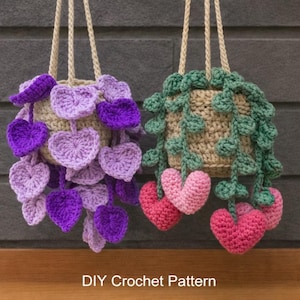 May include: Two hanging crochet plant holders. One is adorned with purple heart-shaped leaves, the other with green leaves and pink hearts. The holders are suspended by beige rope. The text "DIY Crochet Pattern" is at the bottom.