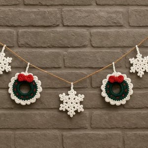 May include: A festive Christmas garland featuring crocheted snowflakes and wreaths. The wreaths are green with white scalloped edges and a red bow. The snowflakes and wreaths are suspended from a natural twine against a brick wall.