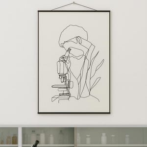 May include: Black framed line art print of a person using a microscope. The artwork is a minimalist illustration in black against a white background. A microscope and lab equipment are visible on a white lab bench below the artwork.