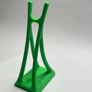 May include: A bright green, 3D-printed stand with a rectangular base and a curved, open design. The stand has a unique shape with two vertical supports that curve inward and meet at the top, creating a holder.